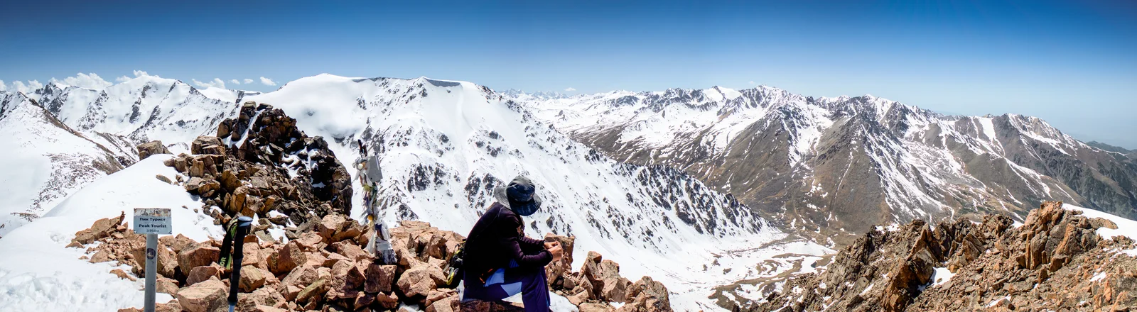A hiker admiring a panoramic view of the snow-covered Tien Shan mountain range